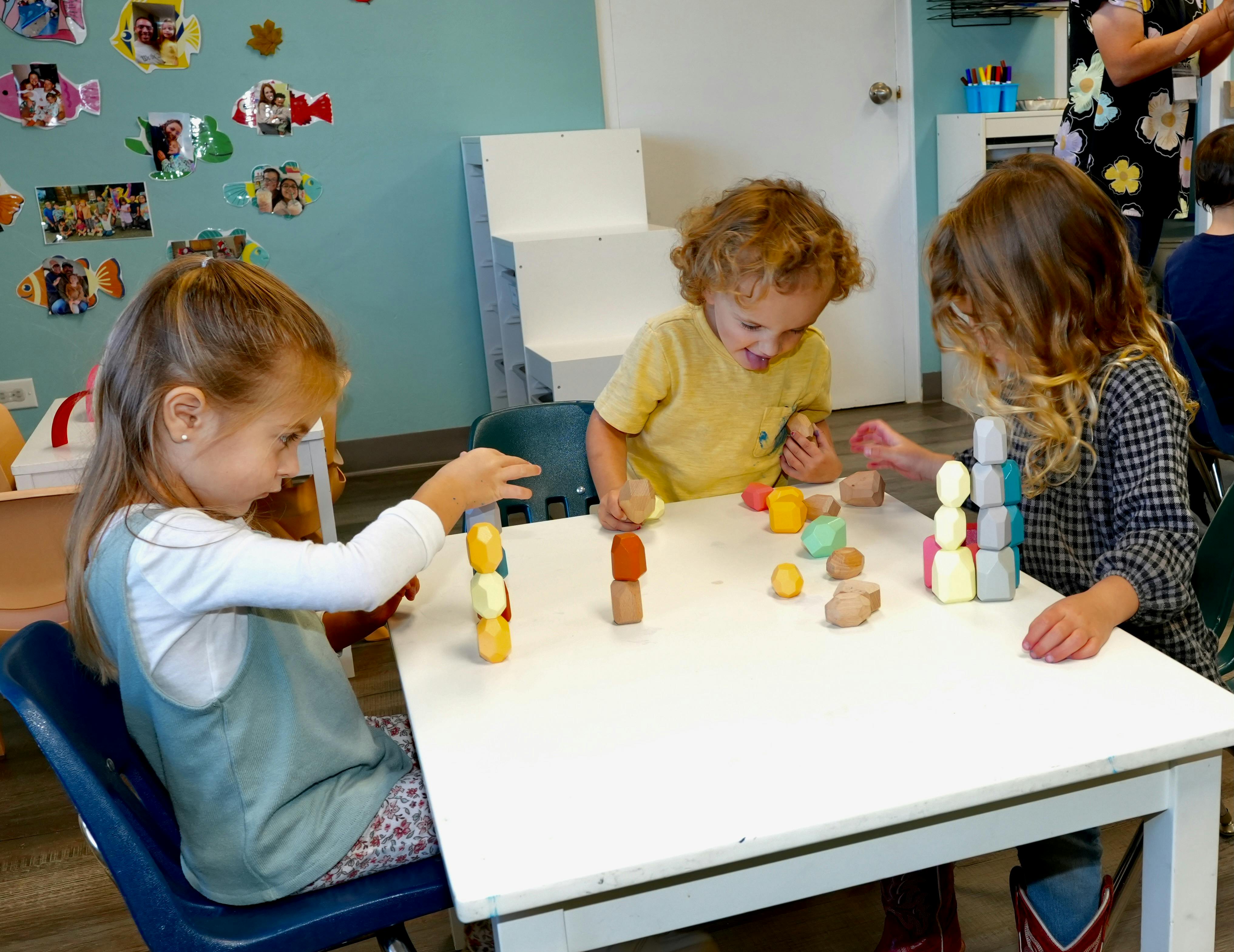 Three children sitting at a table playing with wooden blocks