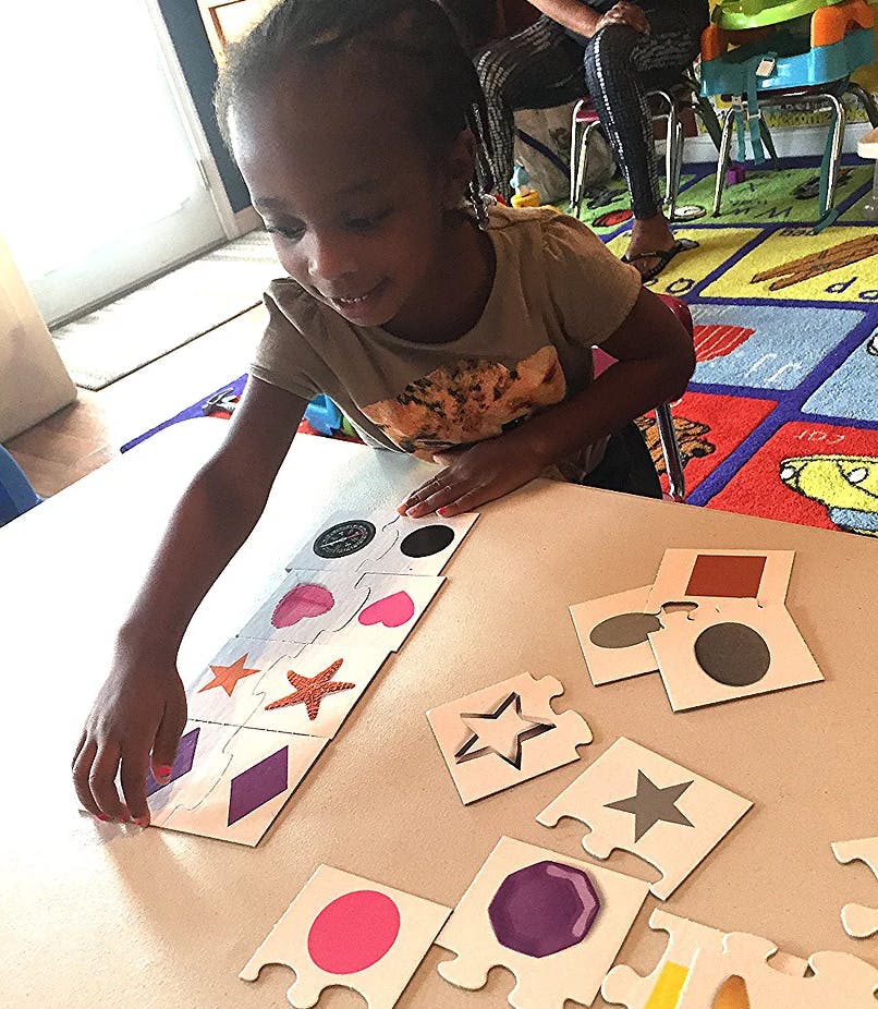 Child playing with shape matching puzzle pieces on a table