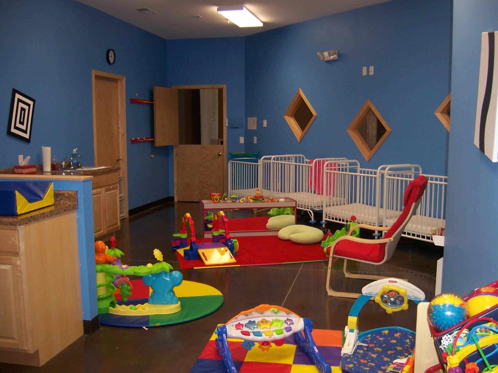 Daycare room with cribs, play mats, and toys
