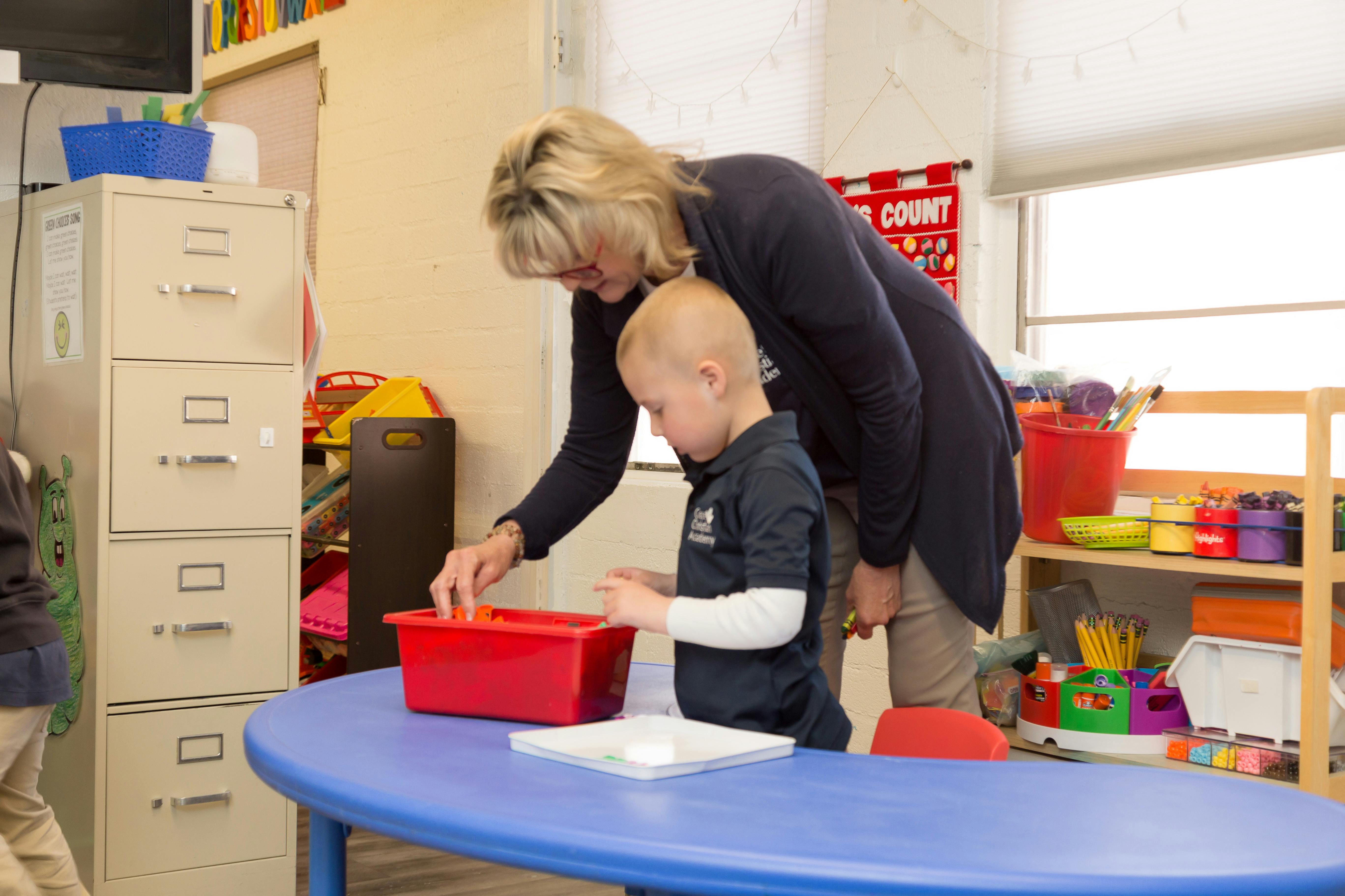 Adult and child interacting with items in a red bin at a table
