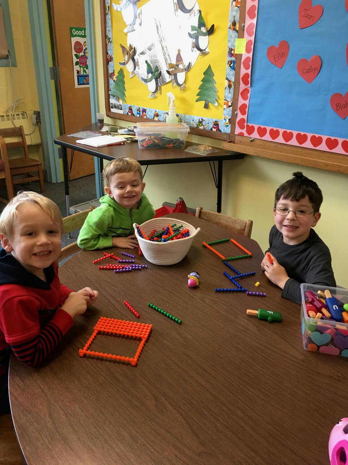 Three children at a table playing with building toys