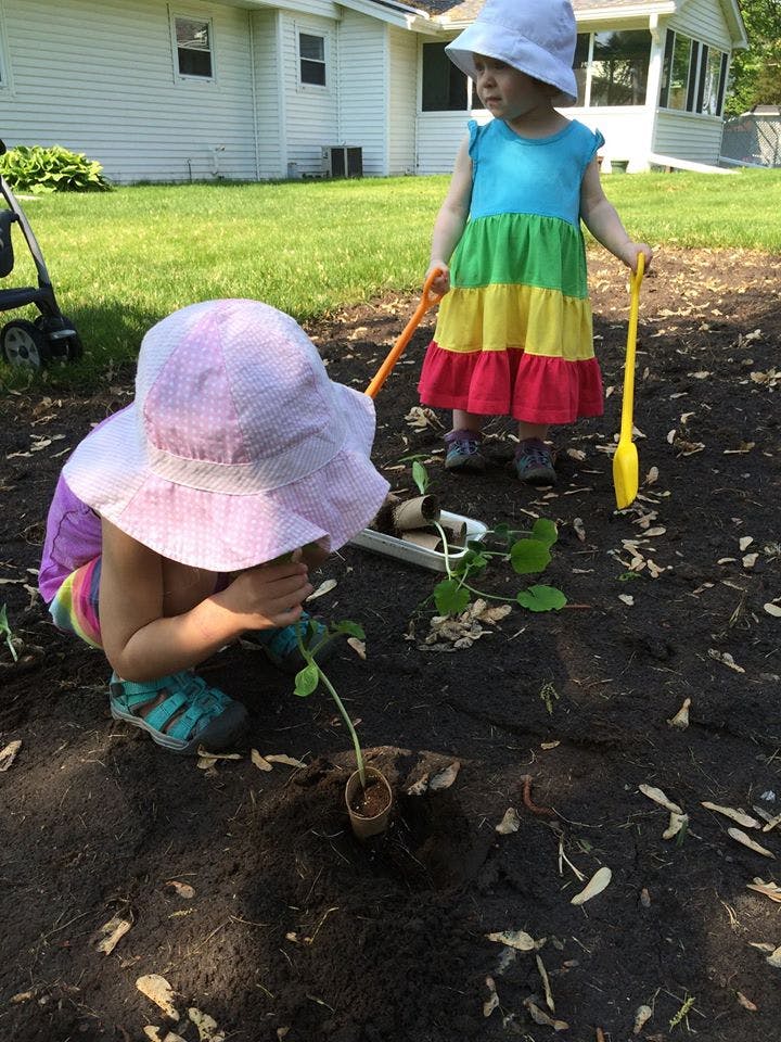 Two children in hats planting in a garden