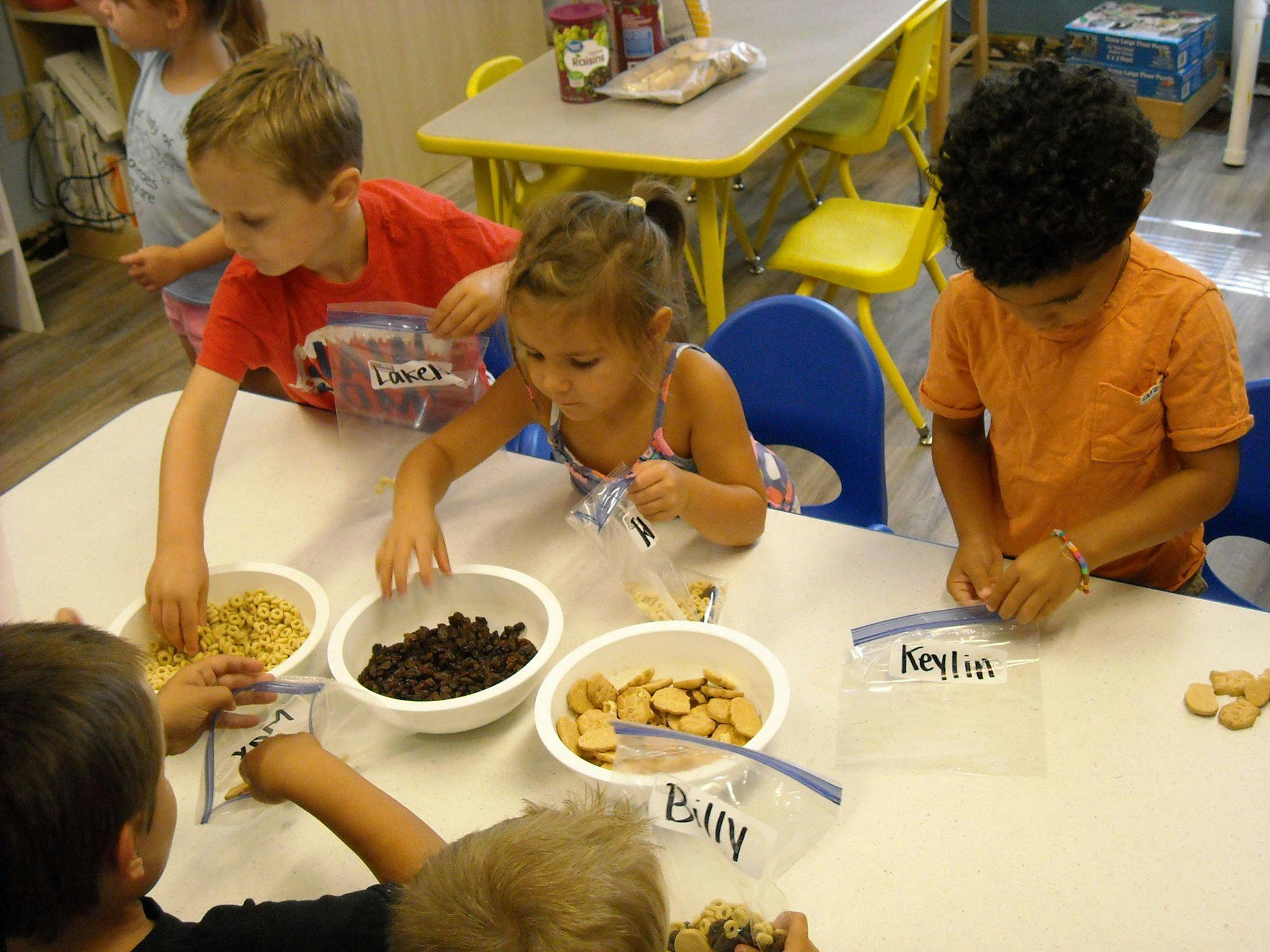 Children putting snacks into plastic bags at a table