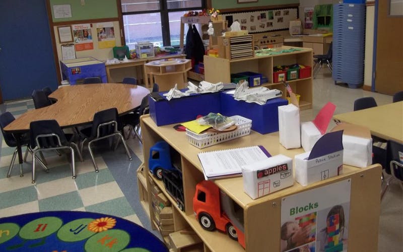 Classroom with child-sized tables and chairs, shelves with toys
