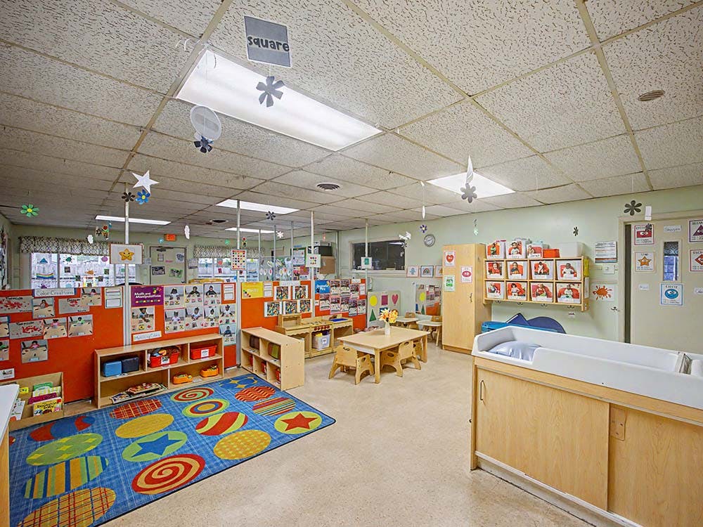 A classroom with a colorful rug, small tables and chairs, and a changing station