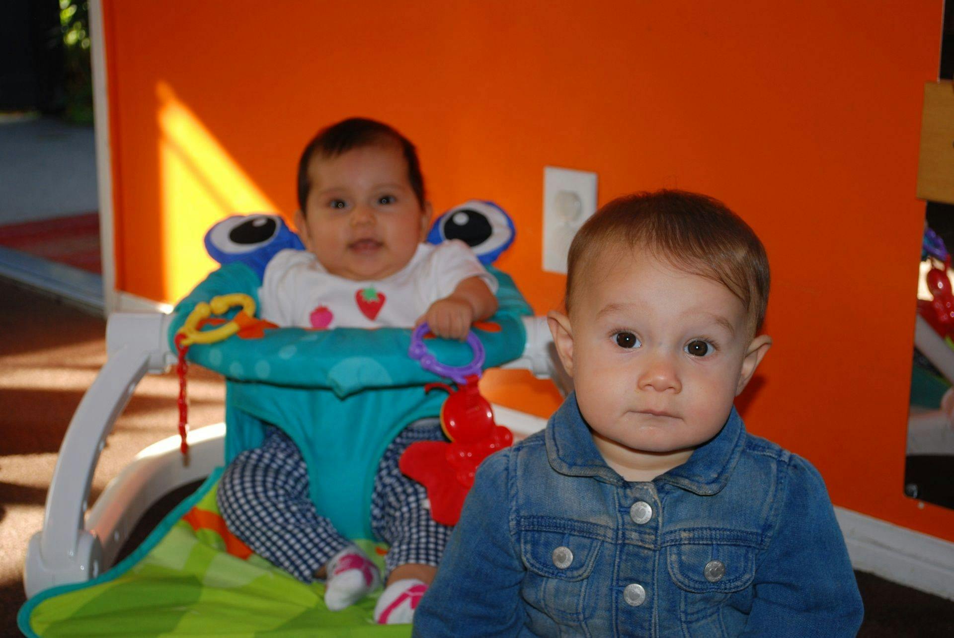 Two babies, one in a bouncer and one in a denim jacket