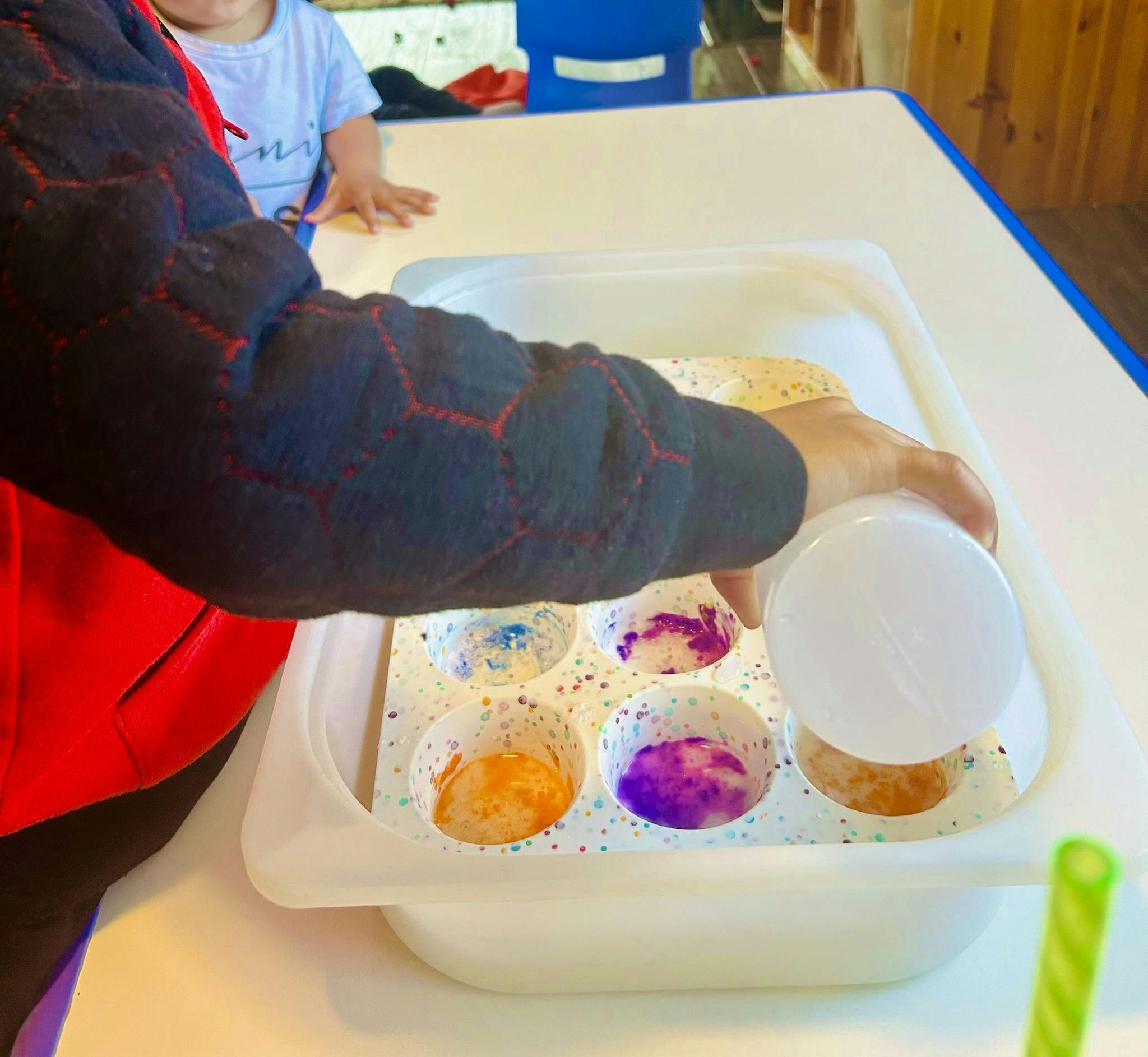 Person pouring liquid into a tray with colorful cups