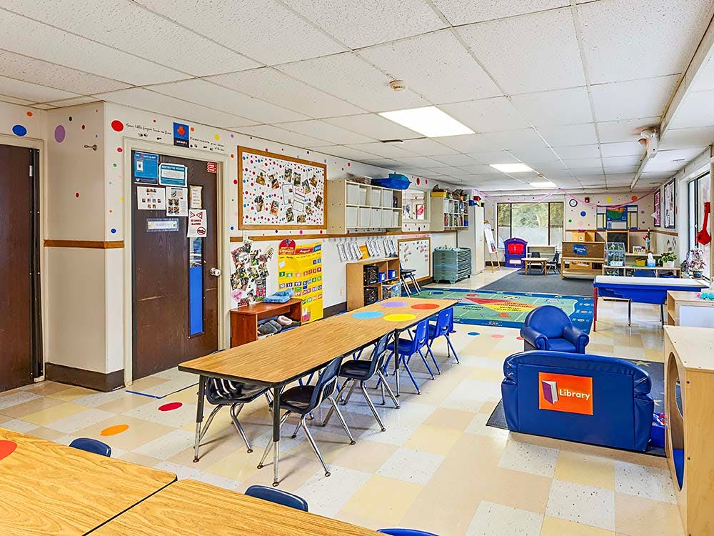 Classroom with child-sized tables and chairs, a play area, and storage shelves