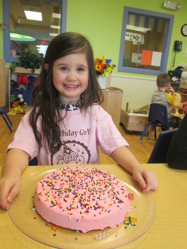Child in a pink shirt with a birthday cake covered in sprinkles
