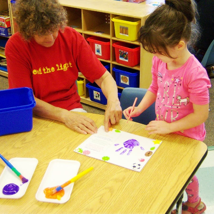 Person and child doing a handprint craft in a classroom