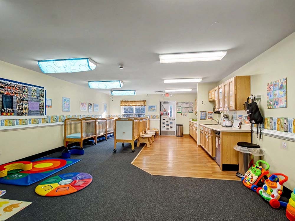 cribs in a daycare room with a kitchen area and play mats