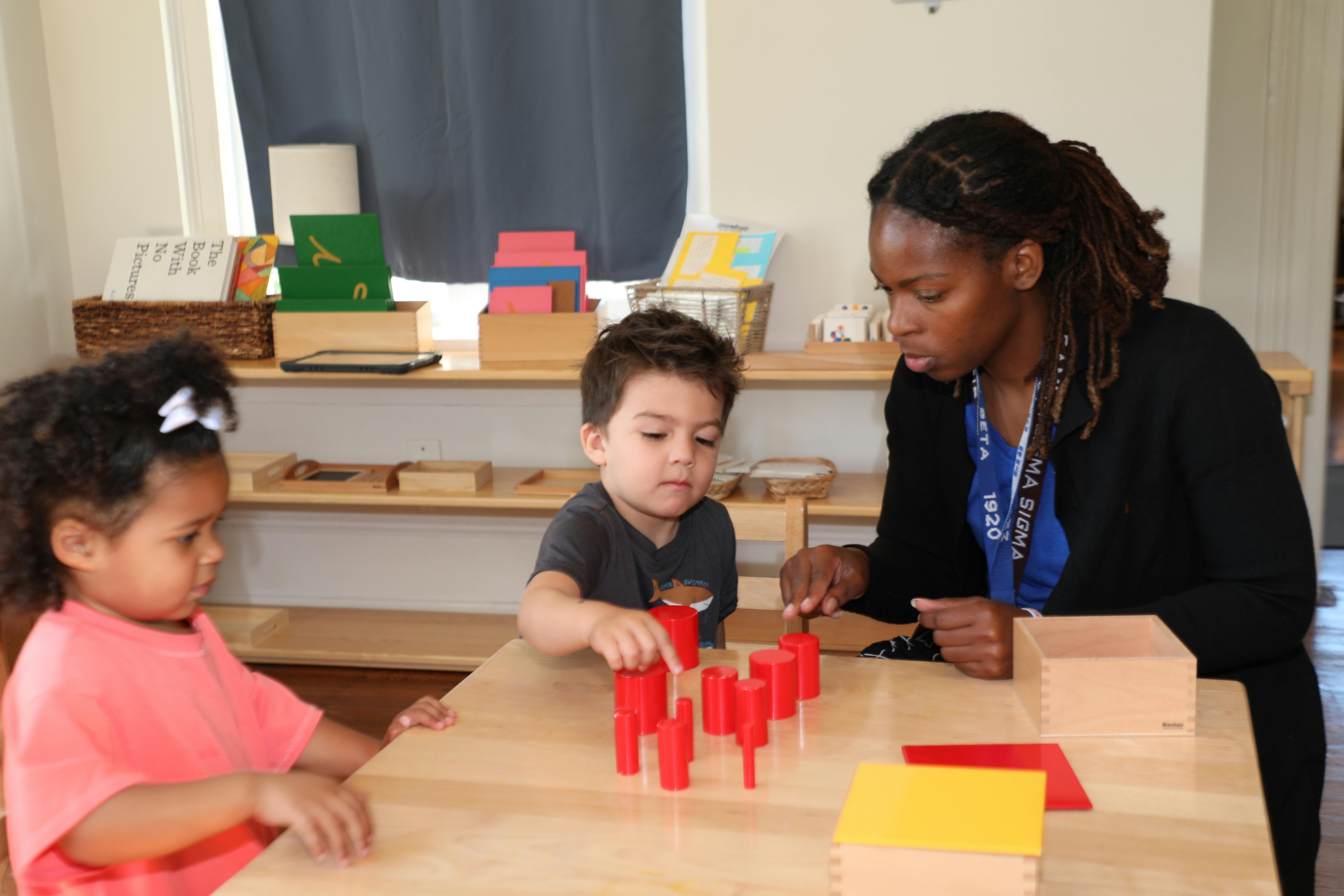 Adult and two children playing with red blocks at a table