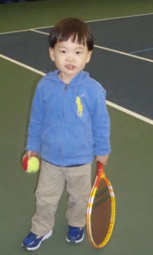 Child holding a tennis ball and a tennis racket