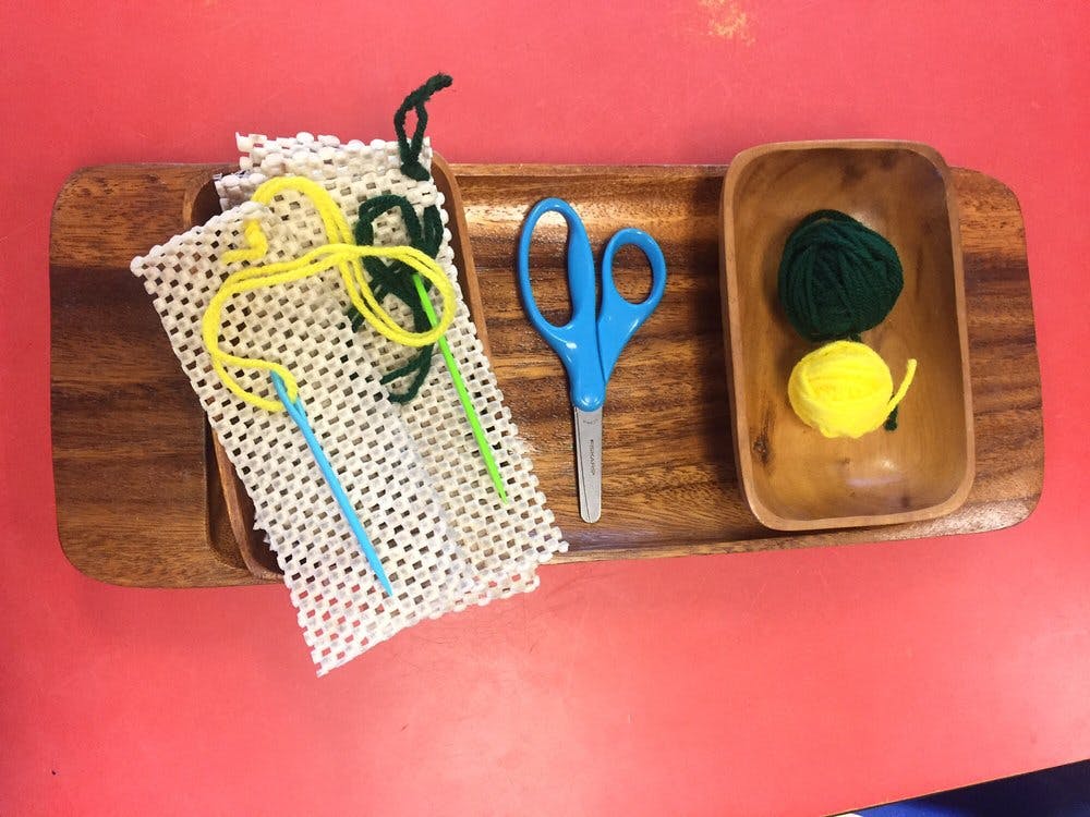 wooden tray with white mesh, yarn, plastic needles, scissors, and yarn balls