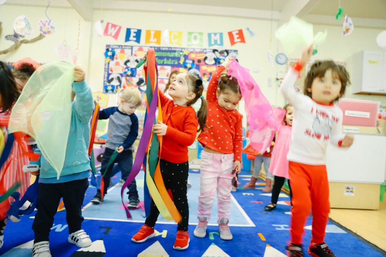 Children playing with colorful ribbons and sheer fabrics in a classroom