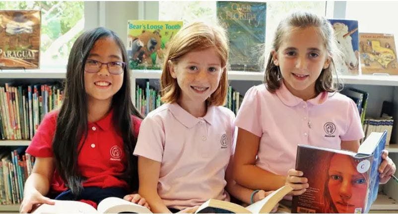 Three children sitting and reading books in a library