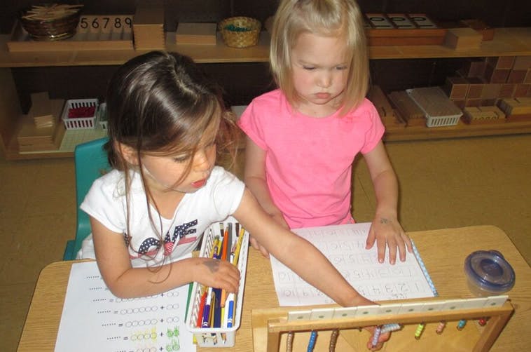 Two children at a desk, one reaching for an abacus