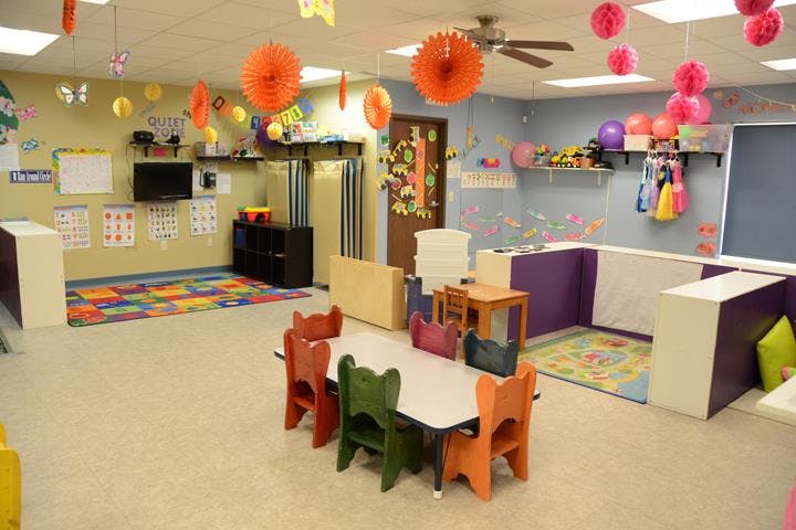 A colorful classroom with small tables and chairs, decorated with paper lanterns