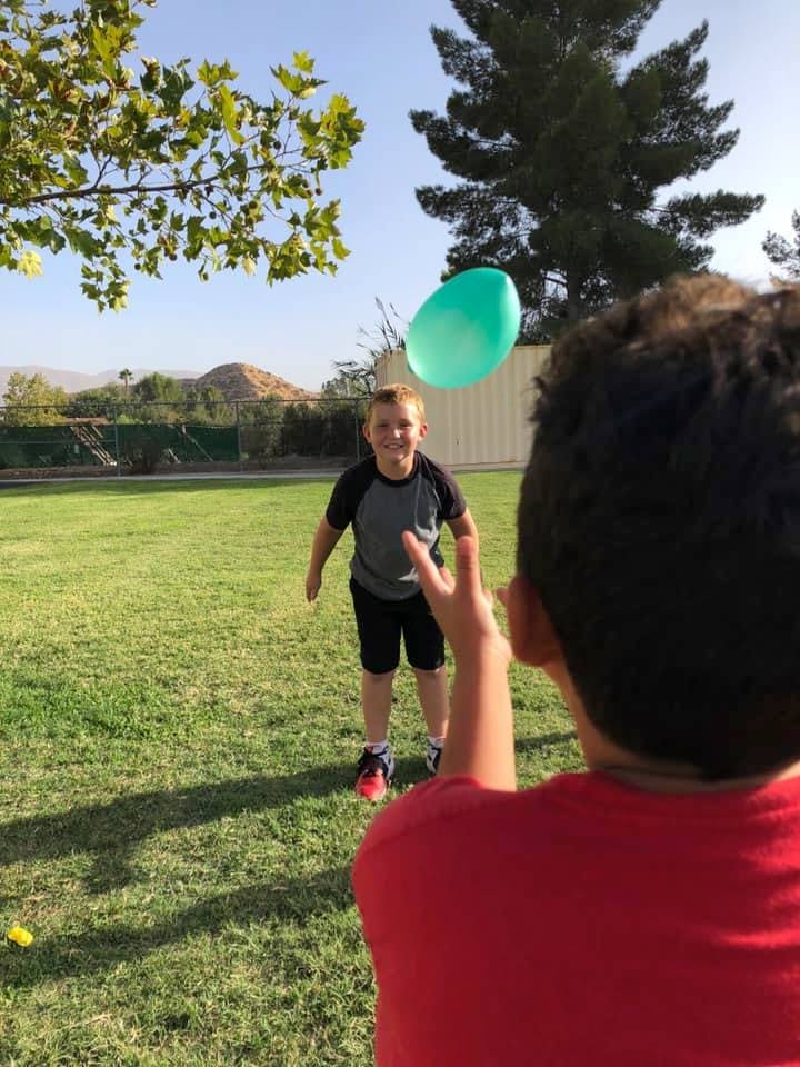 Child throwing a green balloon to another child in a grassy area