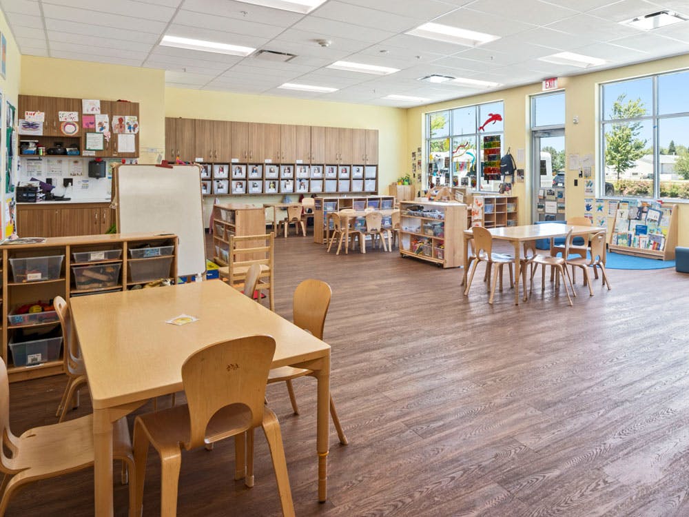 Empty classroom with small wooden tables and chairs, and bright windows