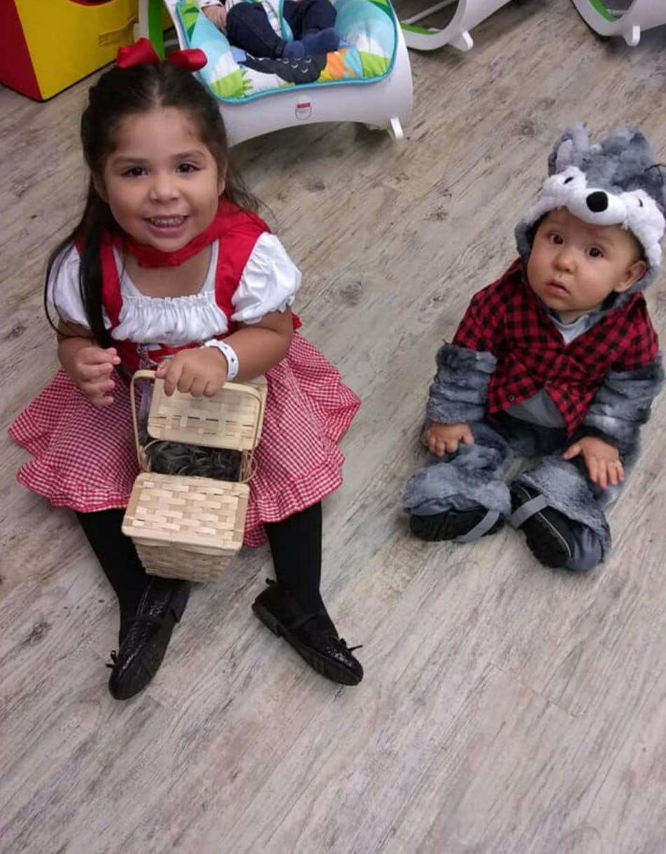 Child in red dress holding basket next to baby in wolf costume