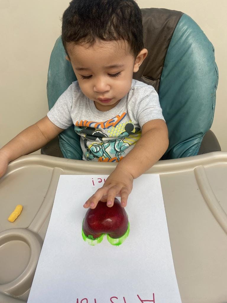 Child in a high chair making an apple print on paper