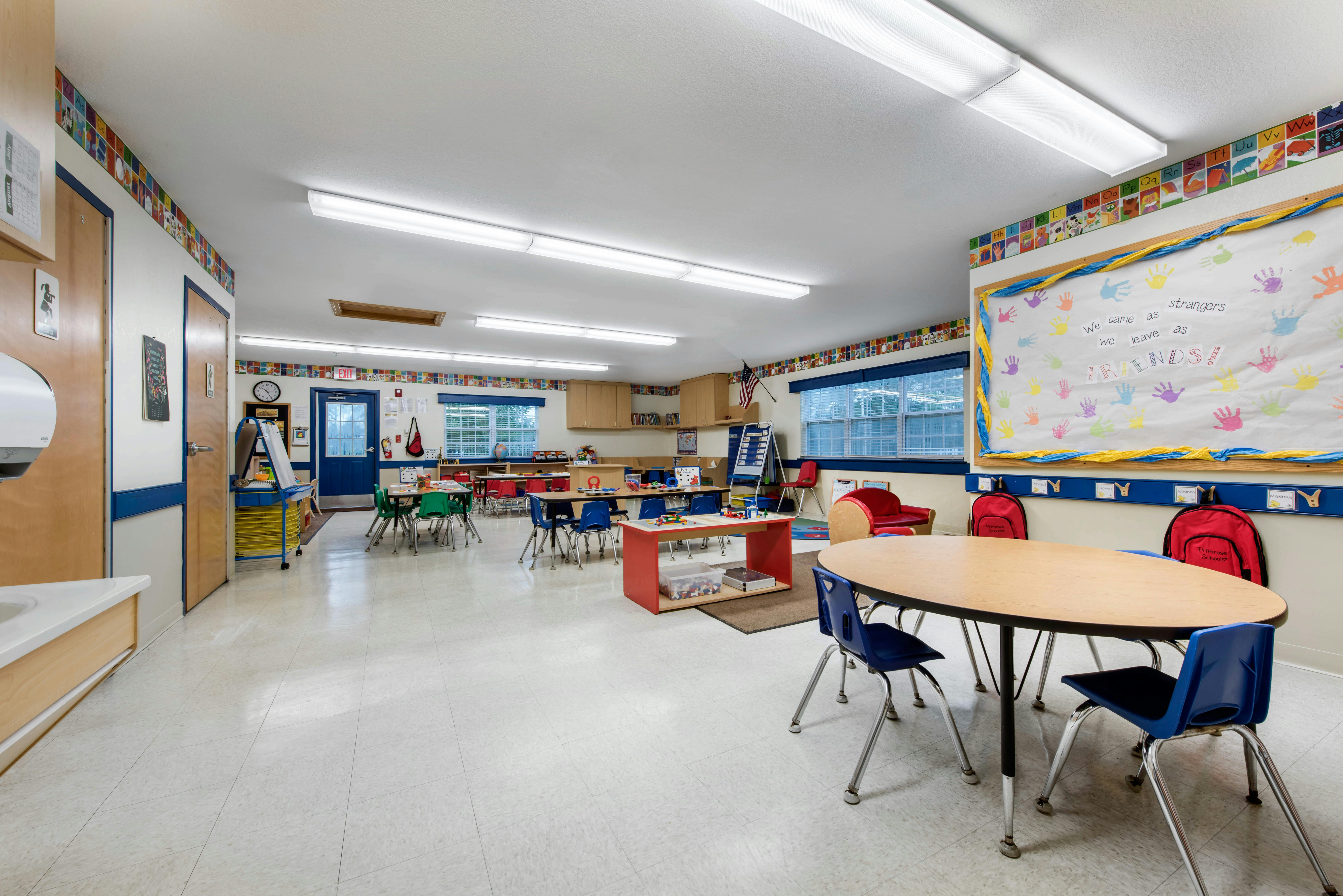 Empty classroom with small tables and chairs, and a whiteboard with handprints