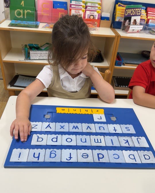 Child placing a magnetic letter on a classroom alphabet board