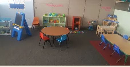 Classroom with small tables and chairs, an easel, and toy shelves