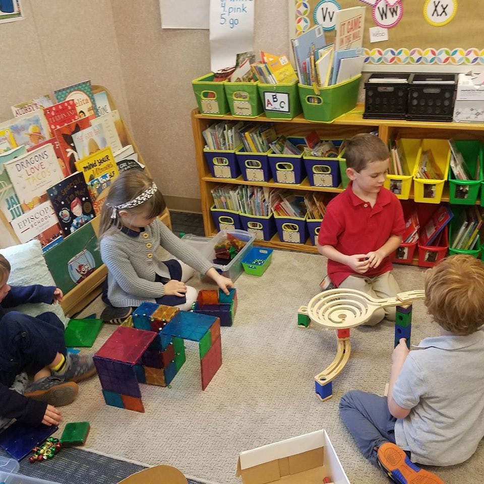 Three children playing with toys on the floor in a classroom