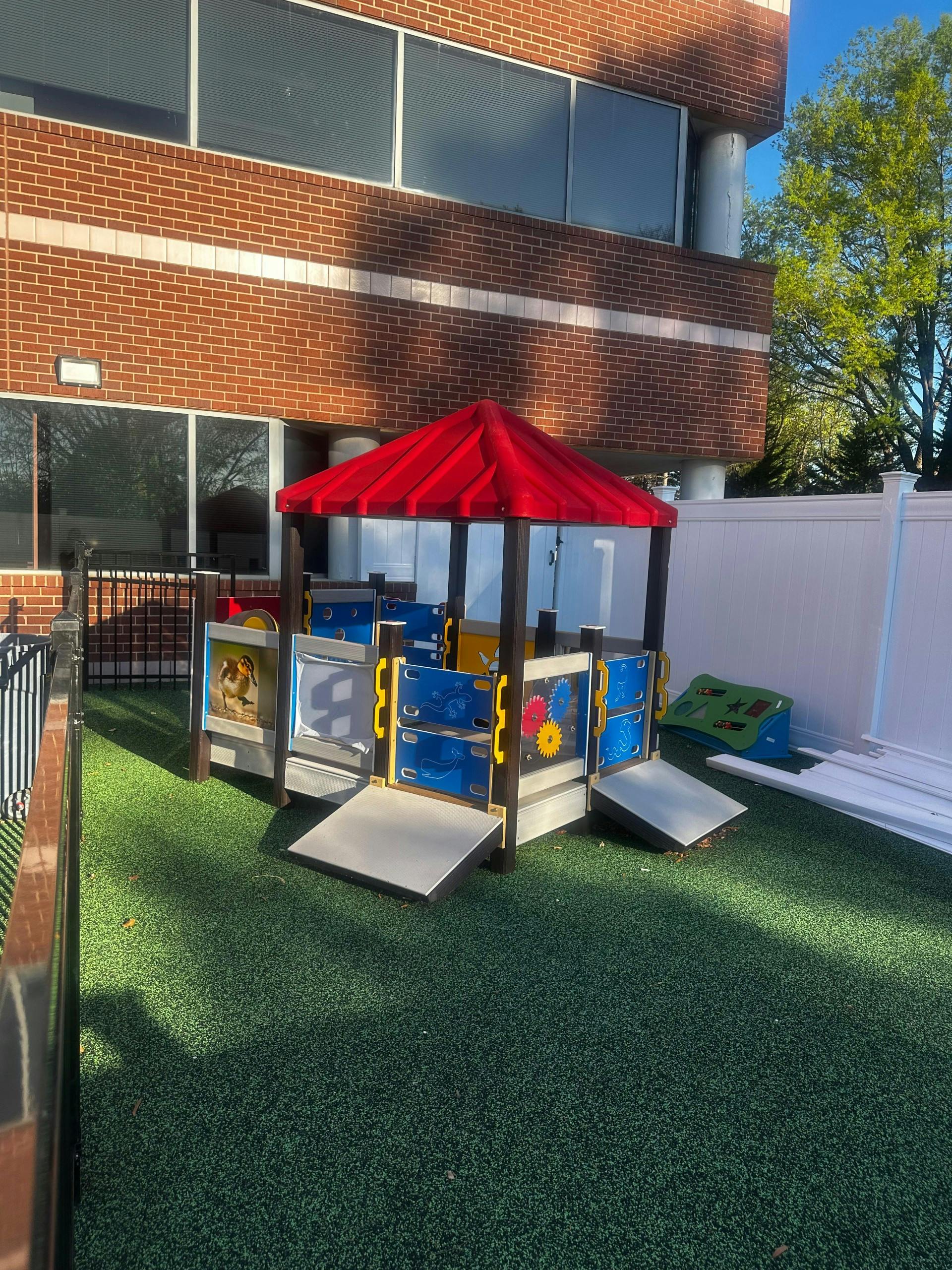 A colorful playhouse structure with a red roof on green artificial turf