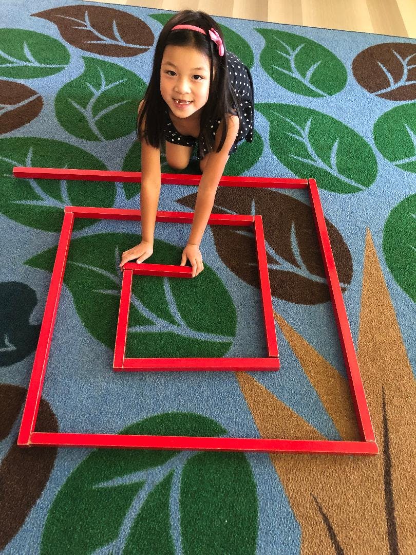 Child on hands and knees on a rug, arranging red square frames