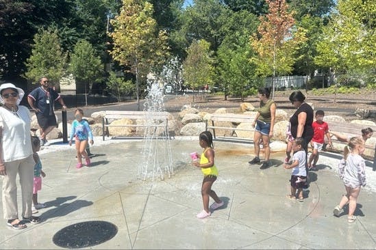 People and children playing in a splash pad with water spraying