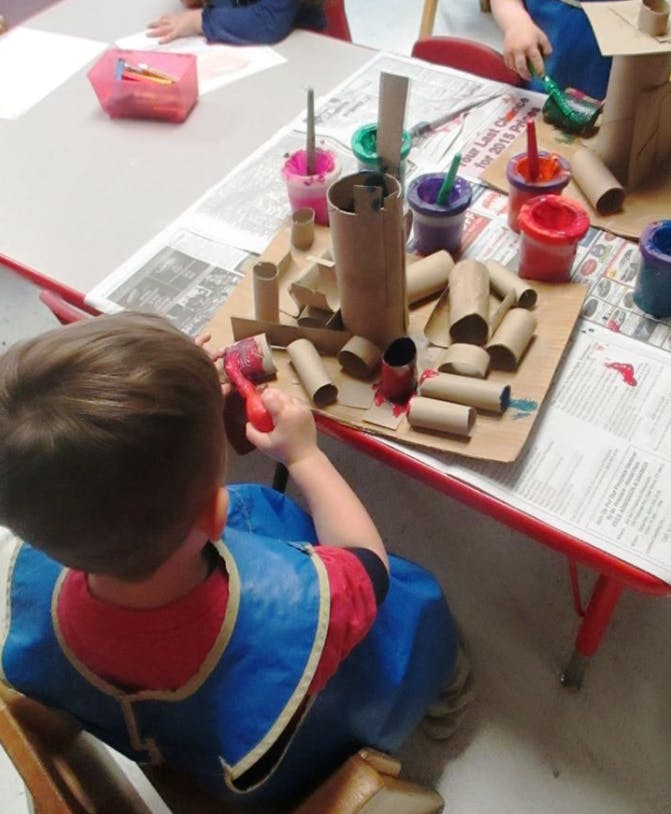 Child painting cardboard tubes at a table