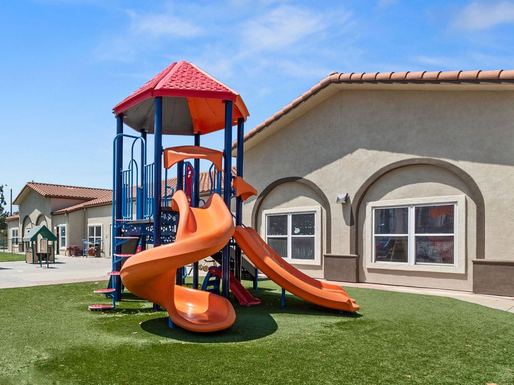 Playground structure with slides on artificial turf next to a building