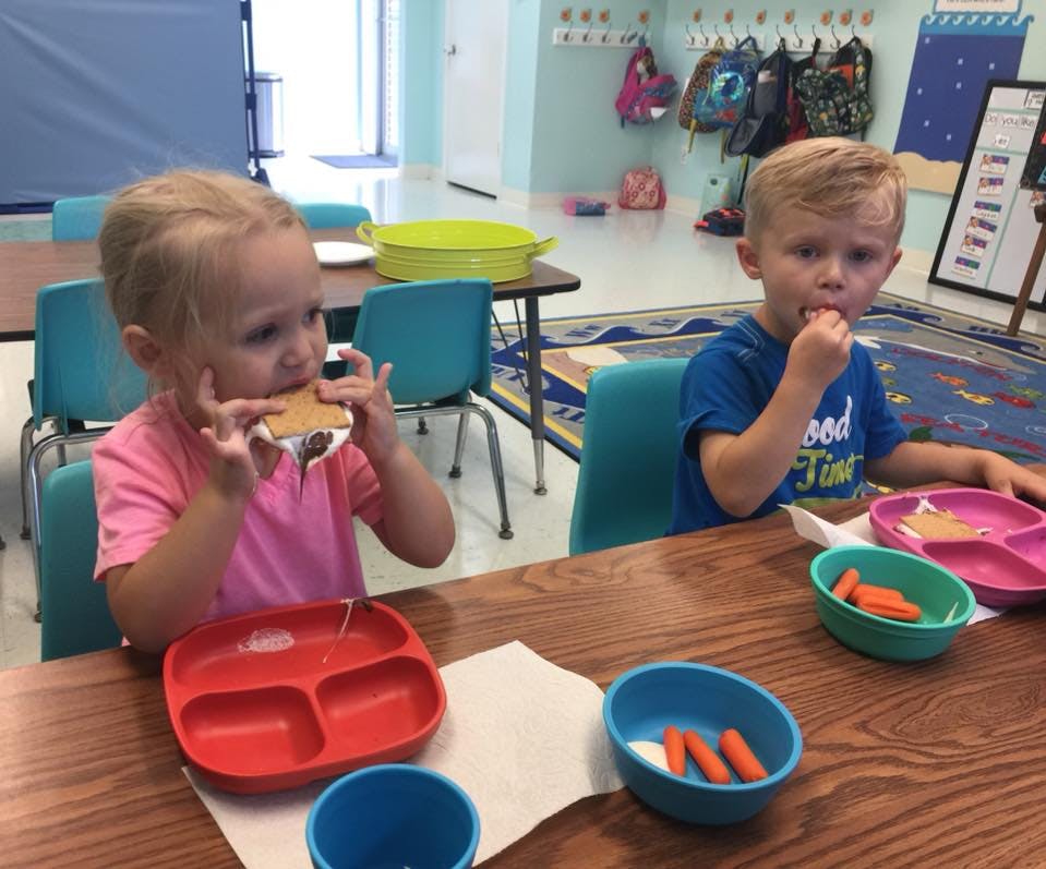 Two children eating at a table in a classroom