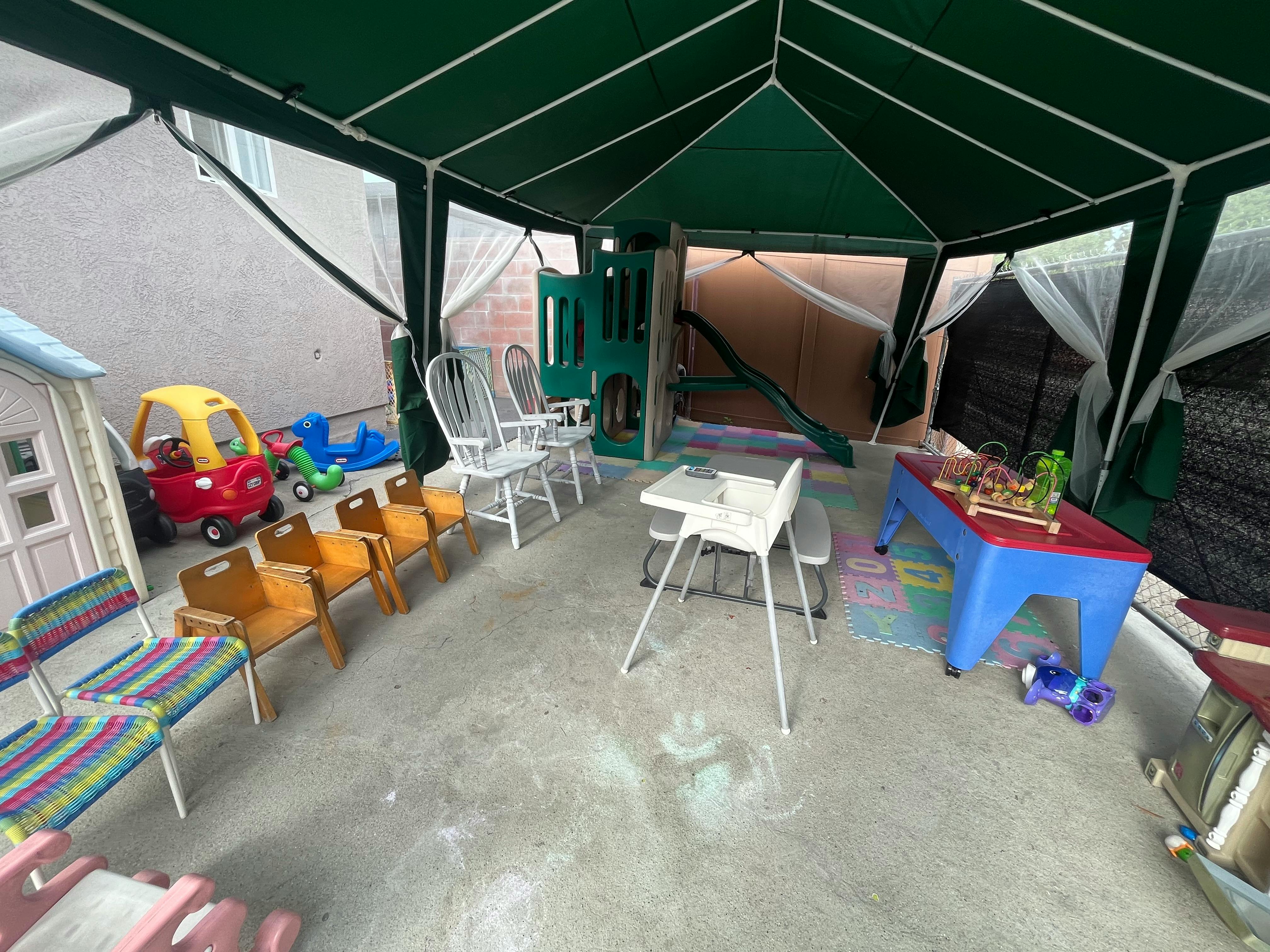 Outdoor play area with small chairs, tables, and toys under a green canopy