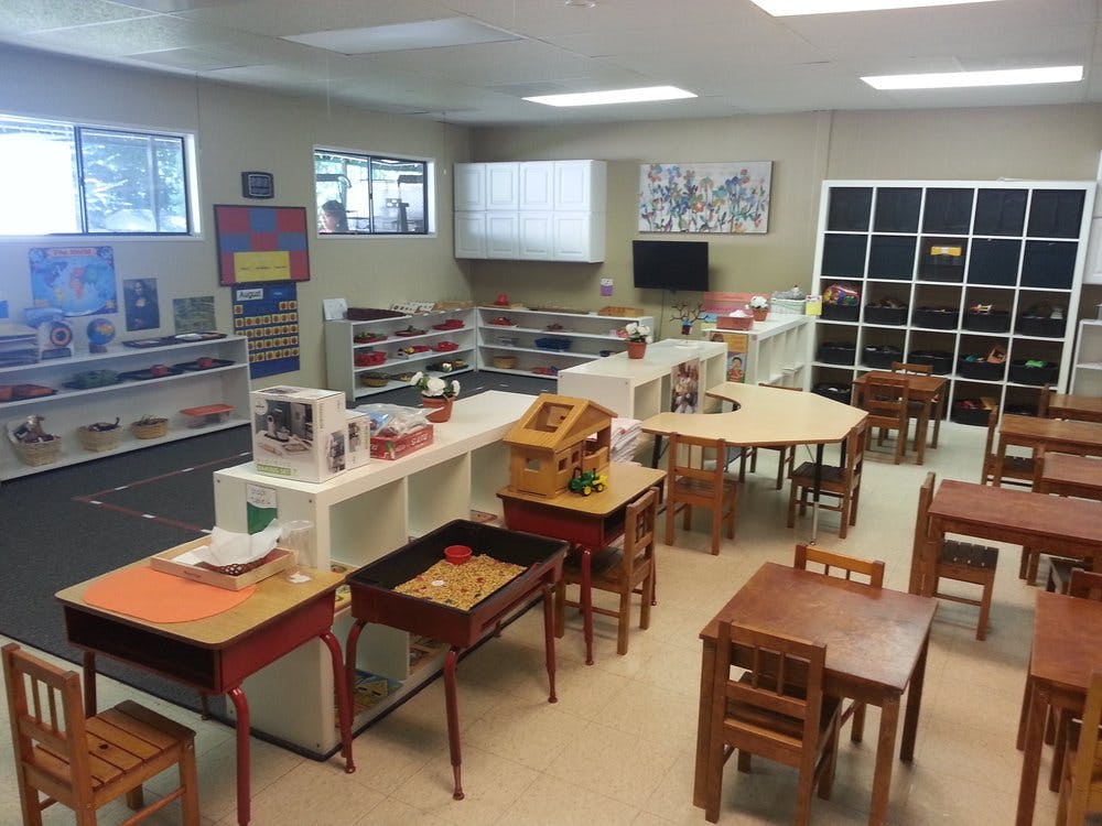 Classroom with small tables and chairs, shelves with learning materials