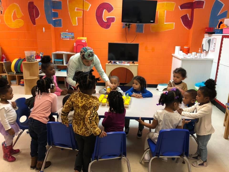 Adult and children gathered around a table in a classroom