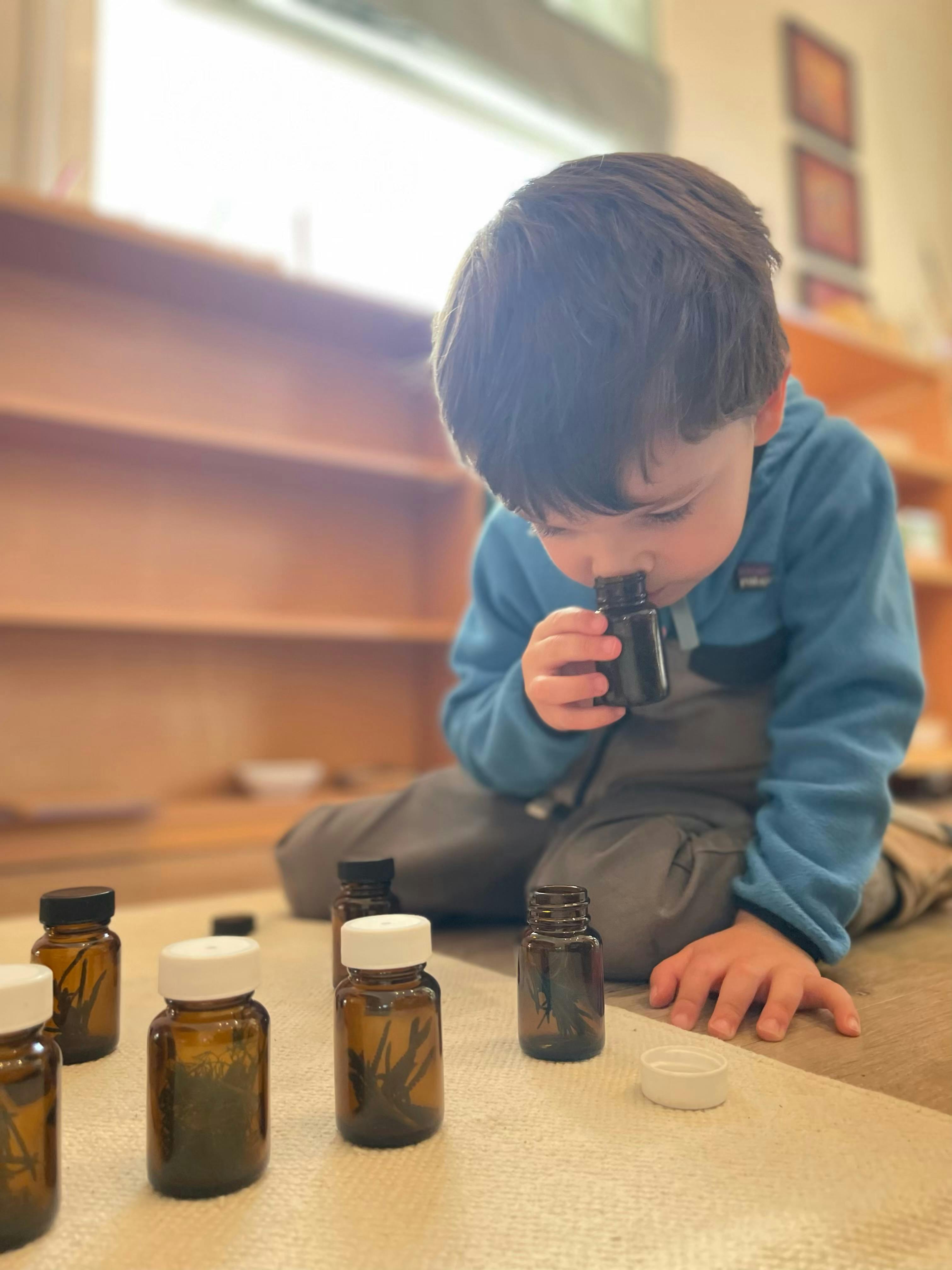 Child smelling a small bottle, surrounded by other small bottles