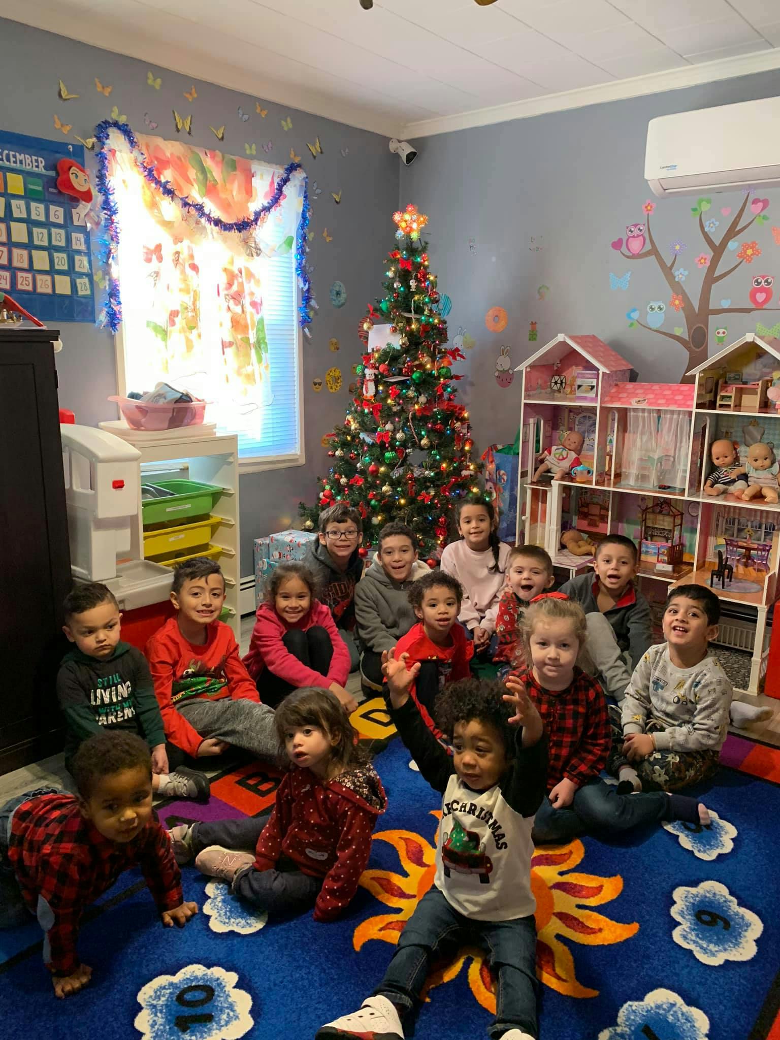 Group of children sitting on a rug in a room with a Christmas tree