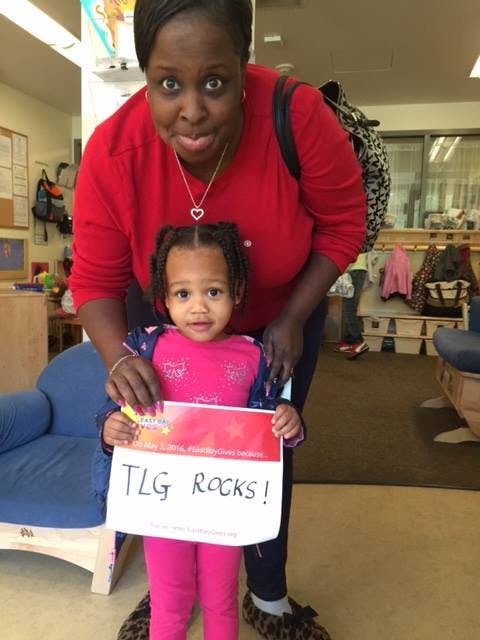 Person and child holding a sign that reads "TLG Rocks!"