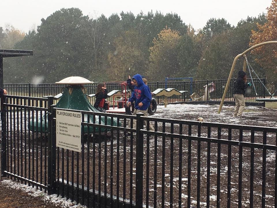 Children playing on playground equipment in light snow