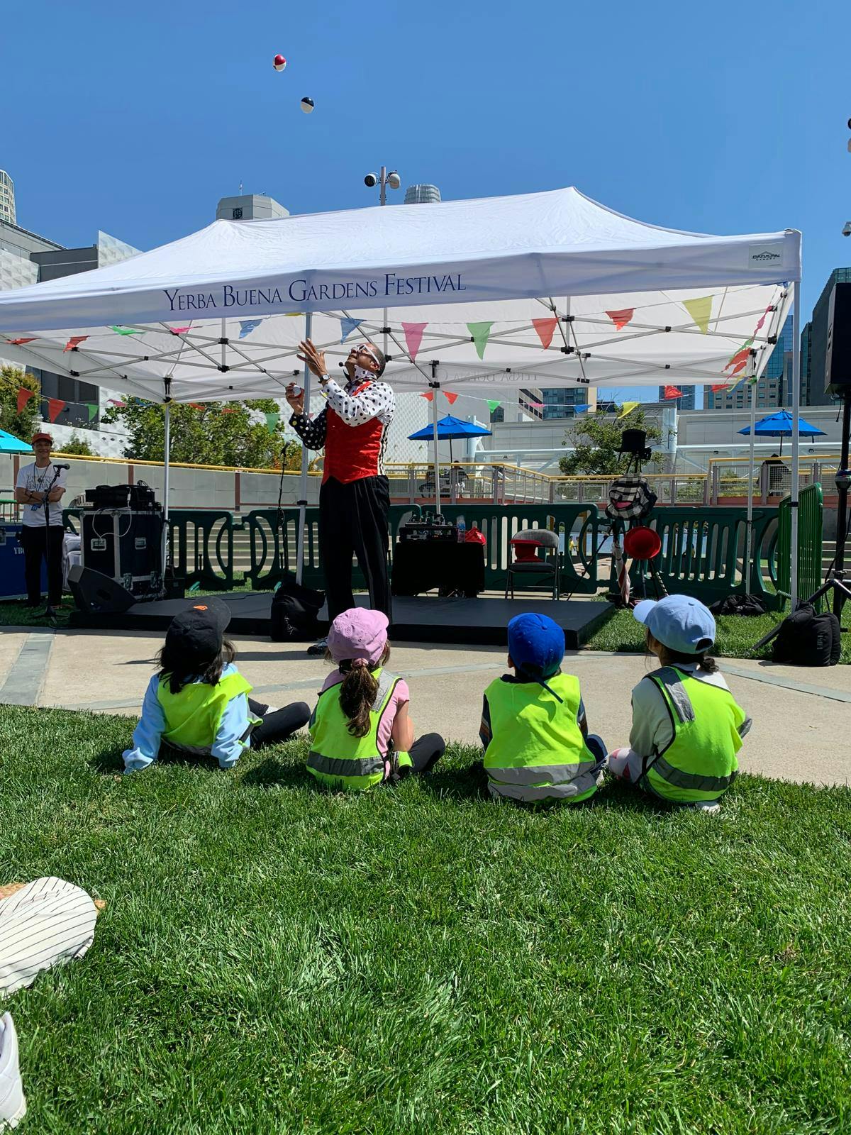 Person juggling under a tent with children watching