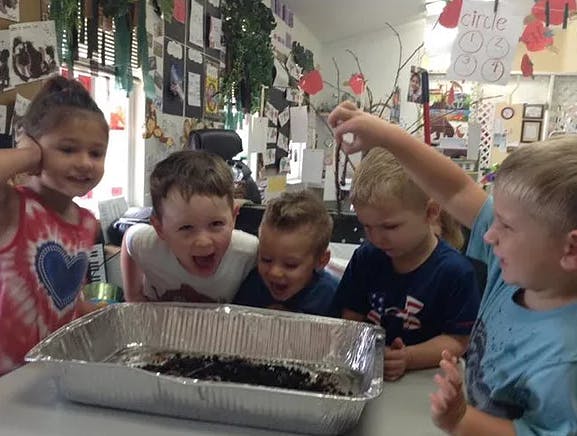 Children gathered around a foil pan with dark contents