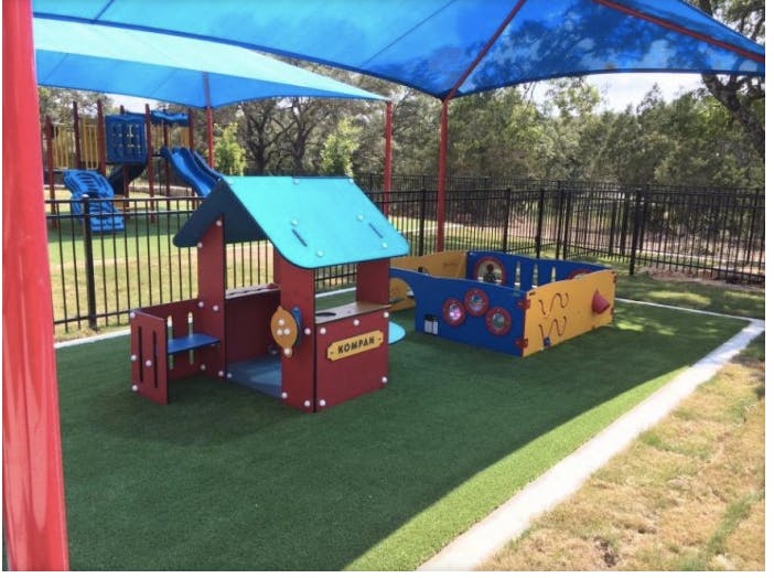 Playground with a small playhouse and sandbox under a blue shade canopy