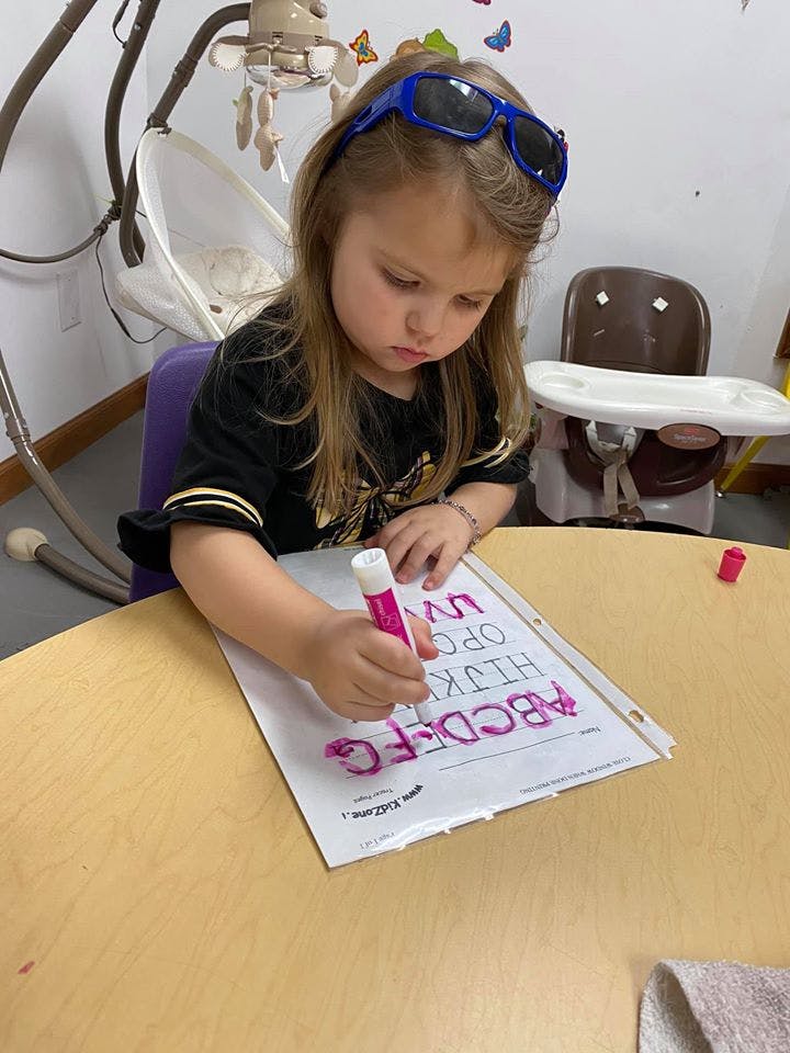 Child with sunglasses on head coloring letters on paper