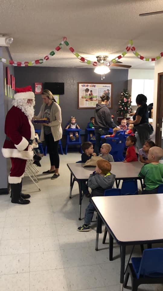 Person dressed as Santa Claus standing near children in a classroom