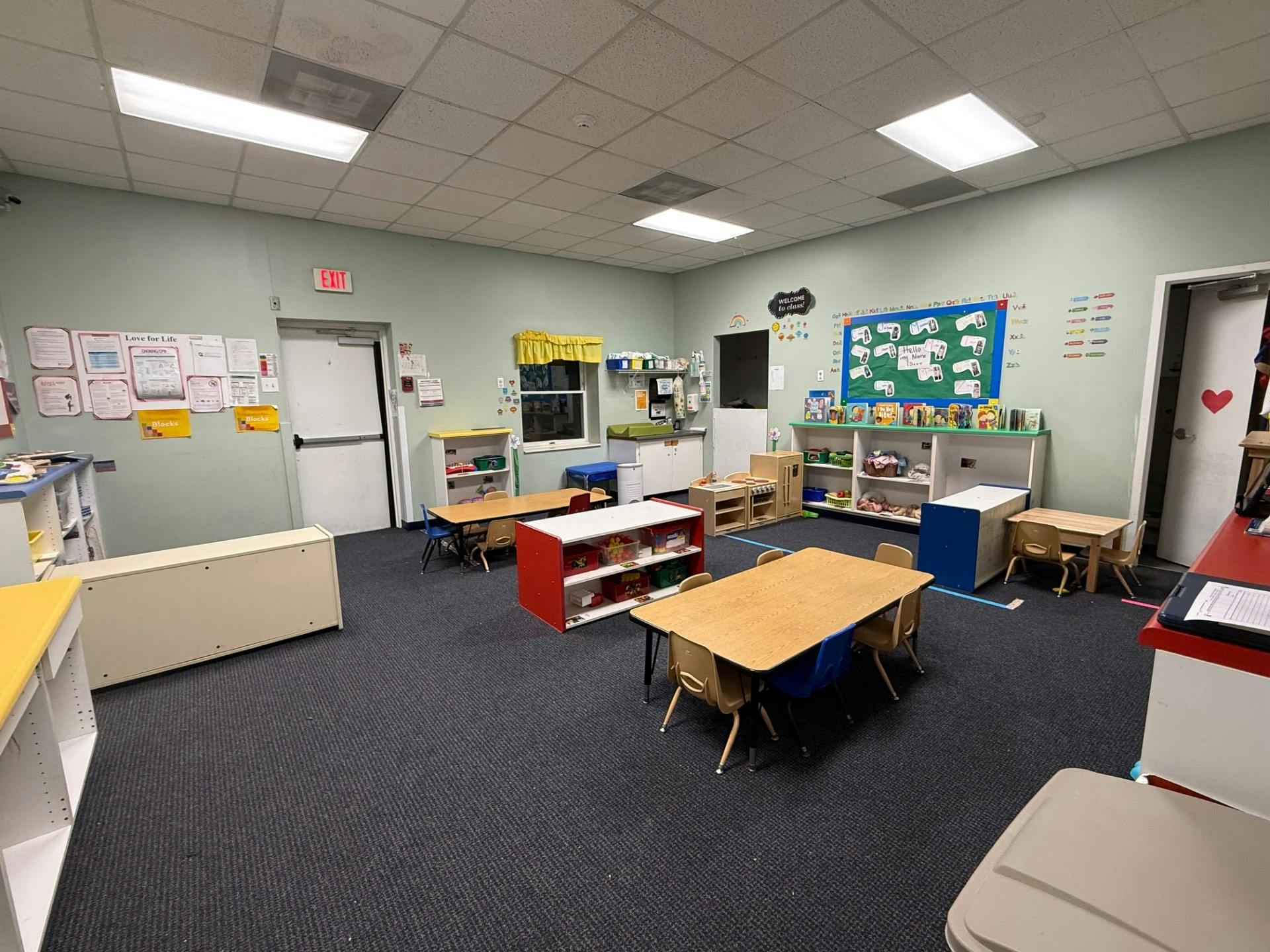 An empty classroom with small tables and chairs, shelves, and learning materials