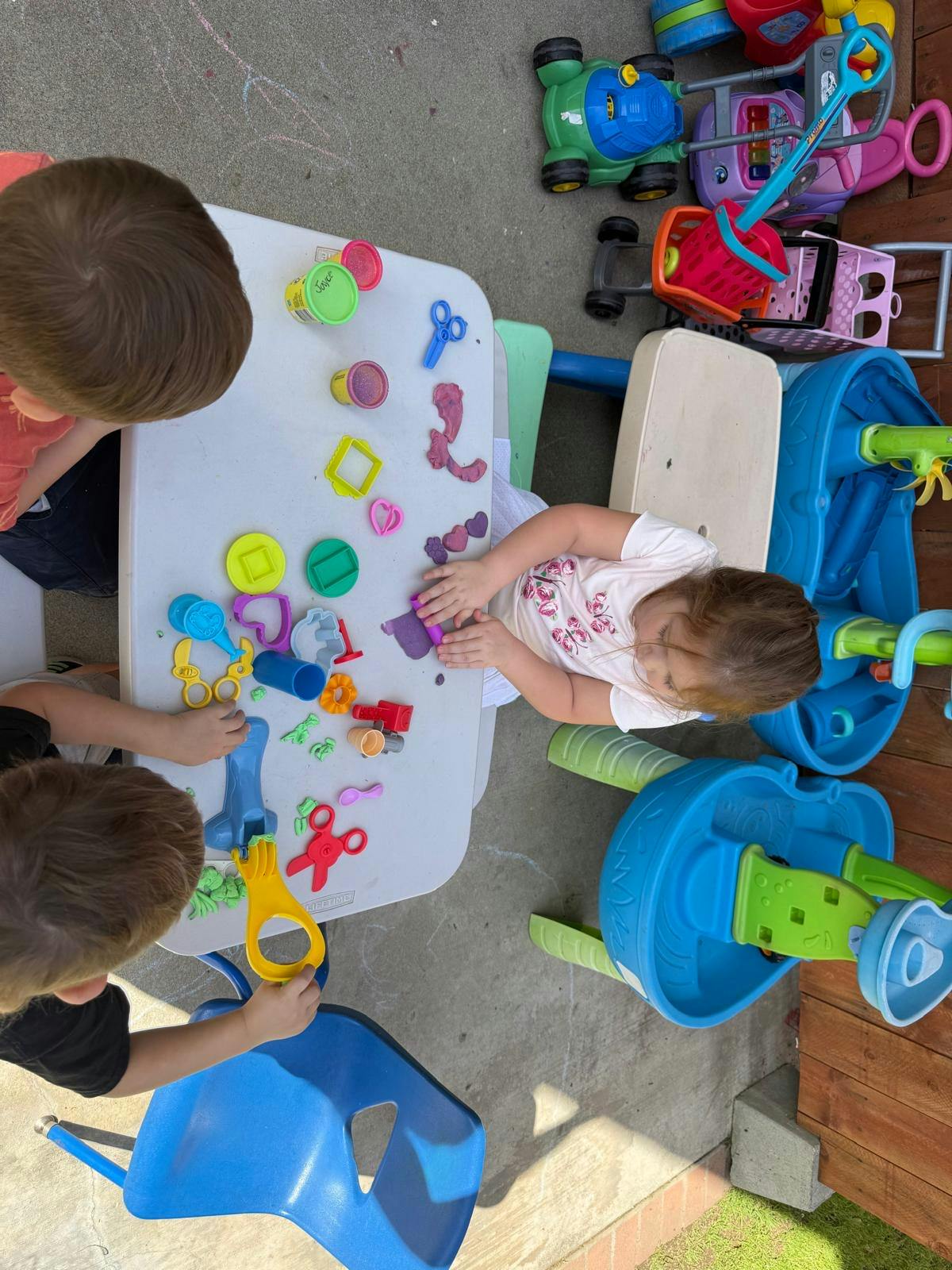 Three children playing with playdough and cookie cutters at a small table
